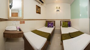 A hotel room with two beds, a small bedside table with a towel and remote control, a mirror, a wall-mounted TV, a framed picture, and a door with a handle. - KG Garden Guest House (Kowloon)
