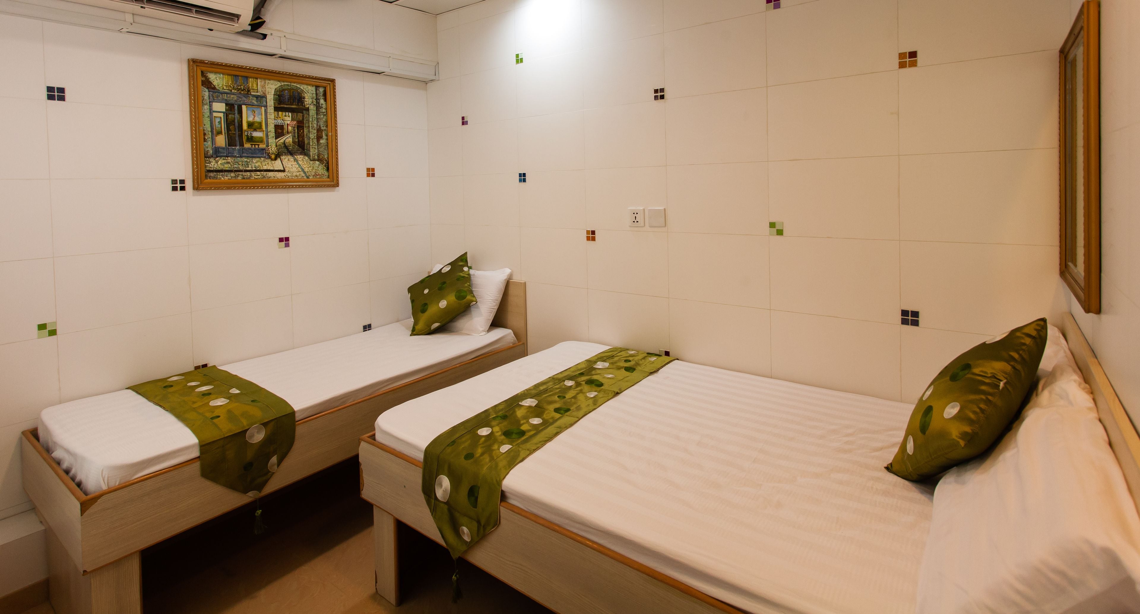 Una habitación con dos camas individuales, cada una con un almohá de color verde y uno blanco. Encima de las camas hay un cuadro en la pared.