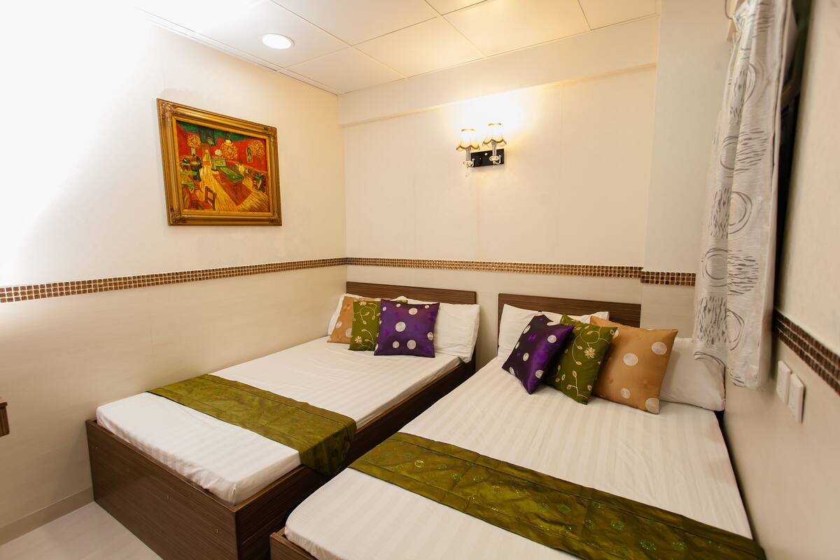 Une chambre d’hôtel avec deux lits simples, chacun recouvert d’une courtepointe verte, agrémenté d’oreillers blancs et de plusieurs coussins à motifs. Un tableau est accroché au mur au-dessus du lit situé à gauche, et un luminaire mural est fixé au-dessus du lit situé à droite.