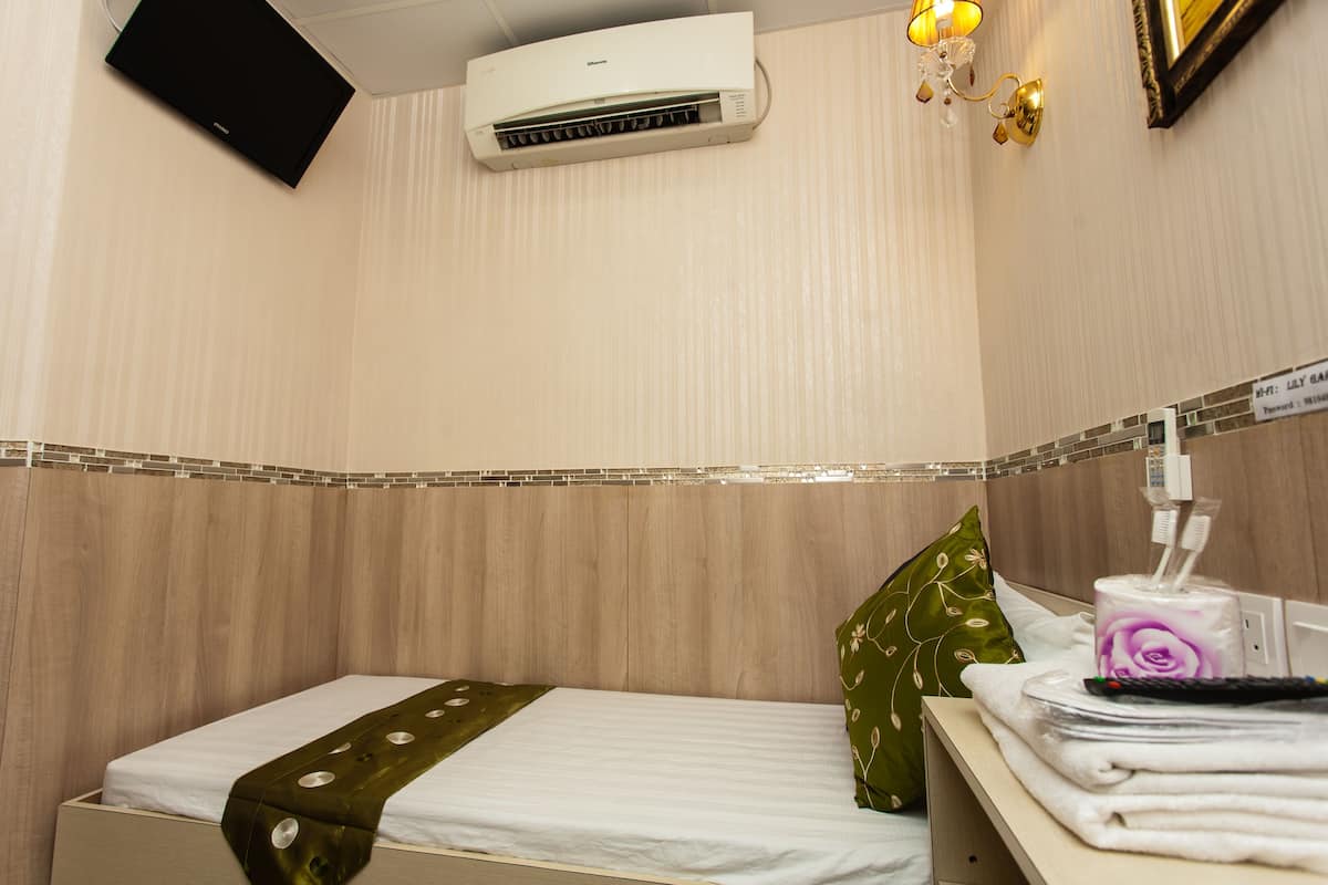 A hotel room with a bed, a nightstand, a wall-mounted air conditioner, a lamp, and a sign indicating Wi-Fi availability.