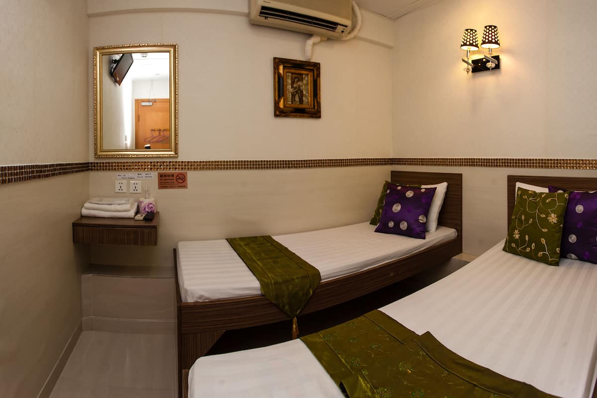 A hotel room with two single beds, a small bathroom with a sink, a mirror, and a wall-mounted air conditioner.