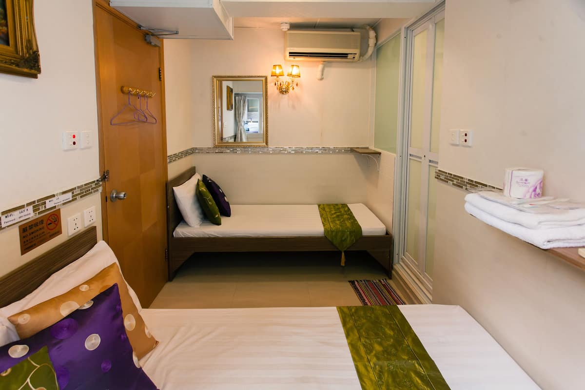 A compact hotel room with a single bed, a small sitting area, a mirror, and a wall-mounted air conditioner.