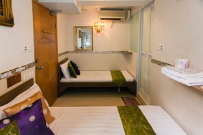 Quarto de hotel compacto com uma cama de solteiro, um pequeno espaço para sentar, um espelho e ar condicionado fixado na parede.
