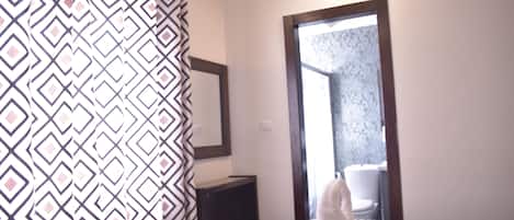 Habitación de hotel con una cortina estampada, un espejo grande, una cama con edredón estampado y vistas a un baño a través de una puerta.