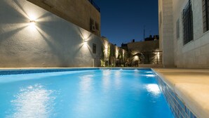 Una piscina con agua cristalina azul, rodeada por un muro bajo y un edificio con fachada de azulejos.