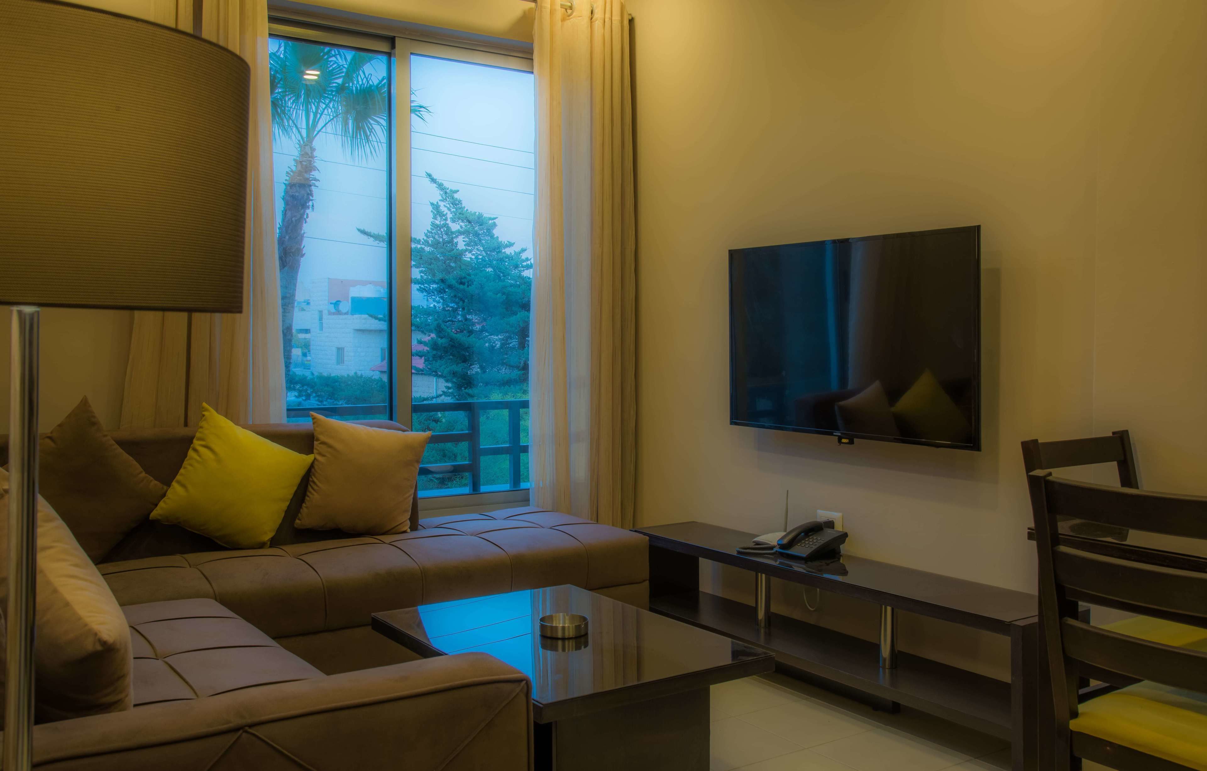 A modern living room with a sofa, a coffee table, a TV mounted on the wall, and a window with curtains.