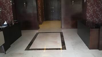 Un vestíbulo de hotel moderno con suelo de mármol, una recepción y una puerta de madera oscura.