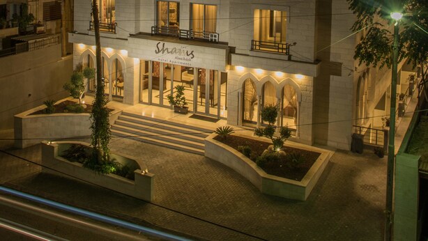 Un hotel con un cartel que dice "Shains Alweibdeh Hotel Apartments" y una entrada bien iluminada con una escalera que lleva a la puerta.
