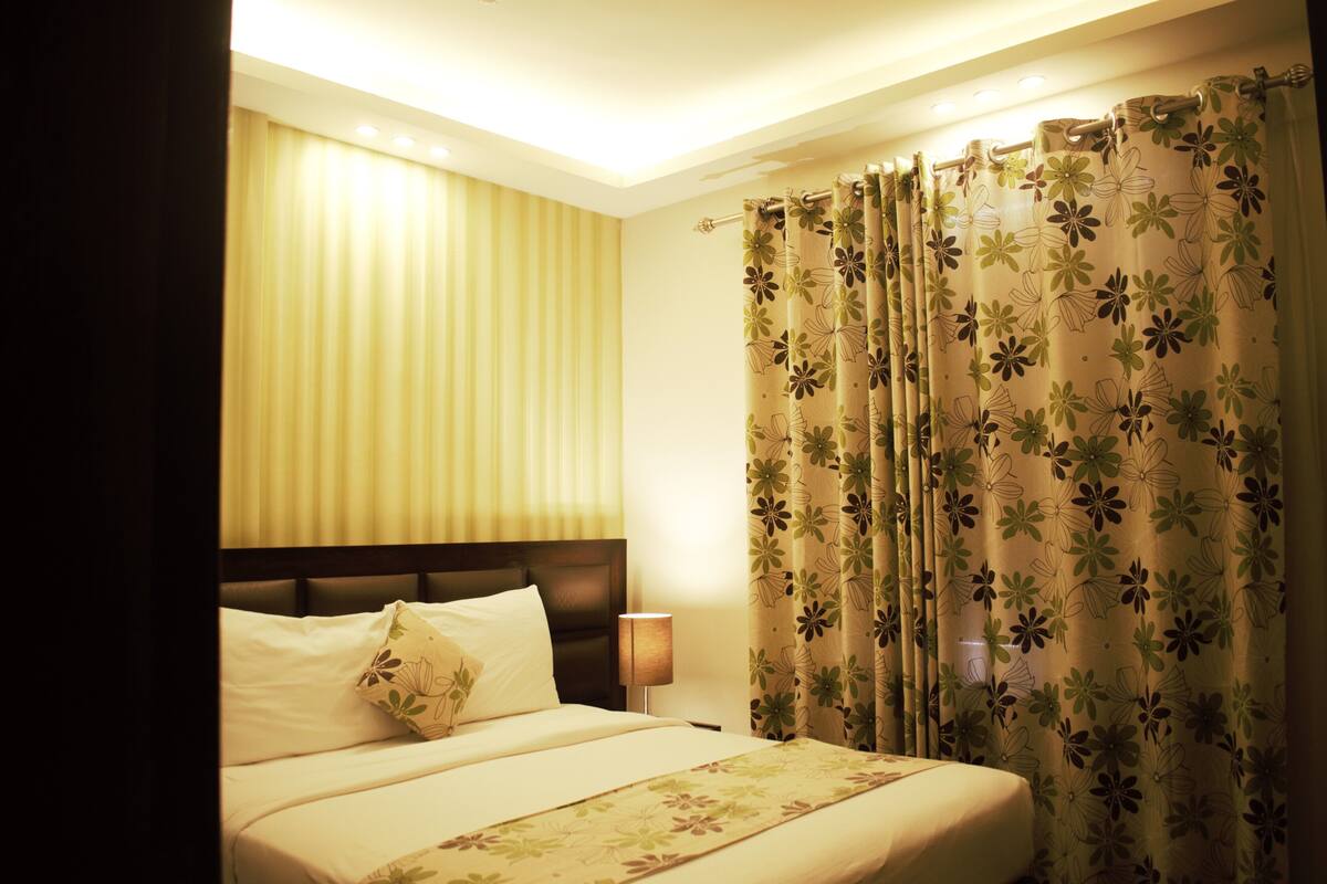 Une chambre d’hôtel avec un lit, des rideaux, une table de chevet et une lampe.