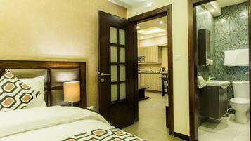 A hotel room with a bed, a wooden door leading to a kitchen, and a bathroom with a marble wall.