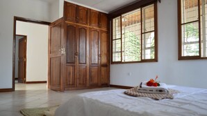 A bedroom with a large wooden wardrobe, a bed with a white bedspread, and a window with a view of greenery. - Villa Poa (Arusha)