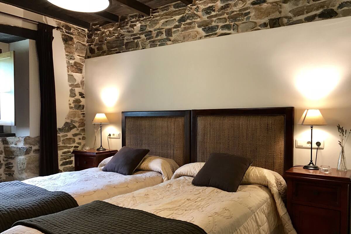 Una cama doble con cabecera, dos mesitas de noche con lámparas y una pared de piedra.