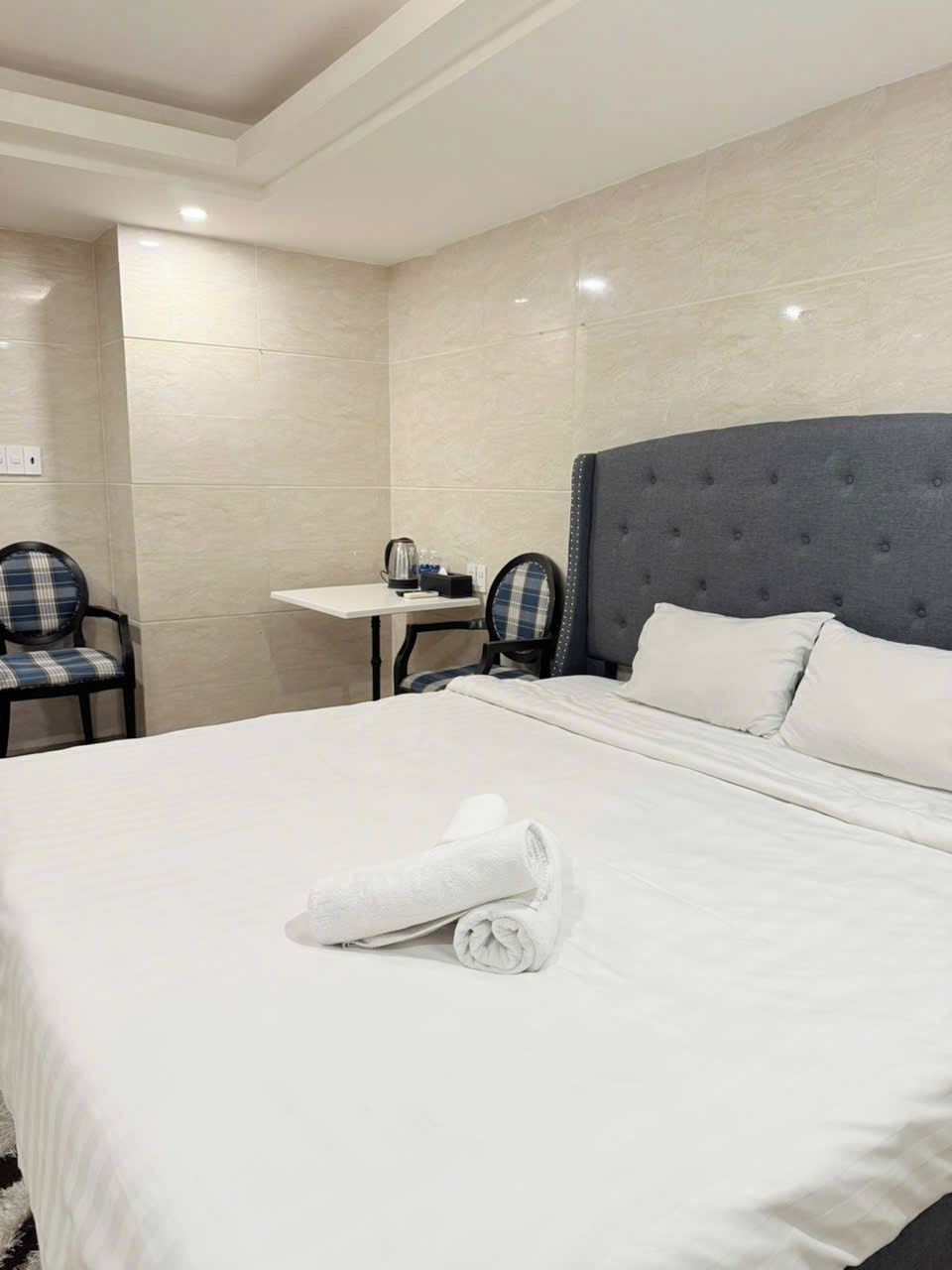 A hotel room with a large bed, a small table, two chairs, and a headboard.