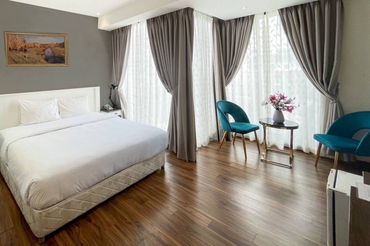 Una habitación de hotel con una cama grande, dos sillas, una mesita con flores y un cuadro en la pared.