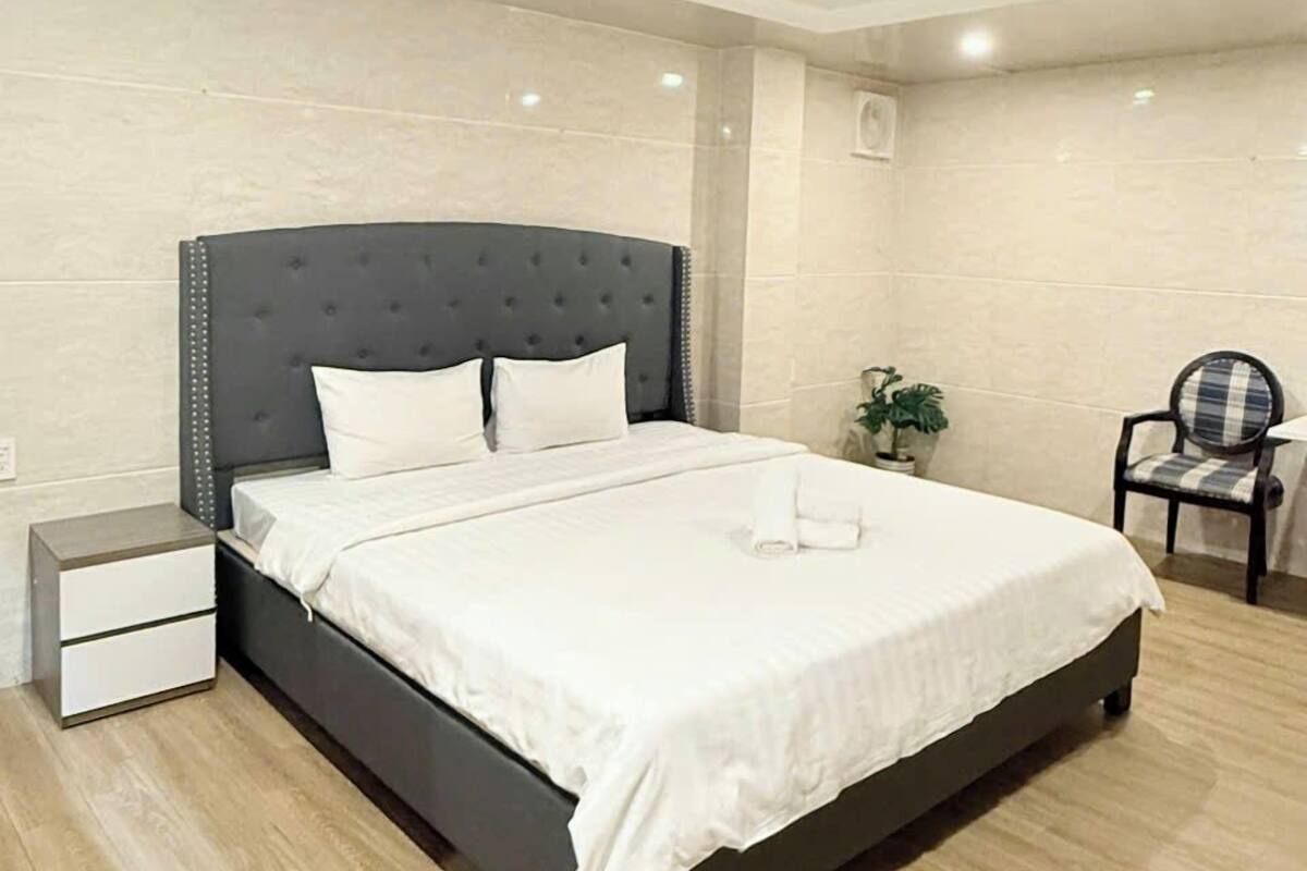 Un dormitorio moderno con una cama grande, una mesita de noche, una silla y una planta en maceta.
