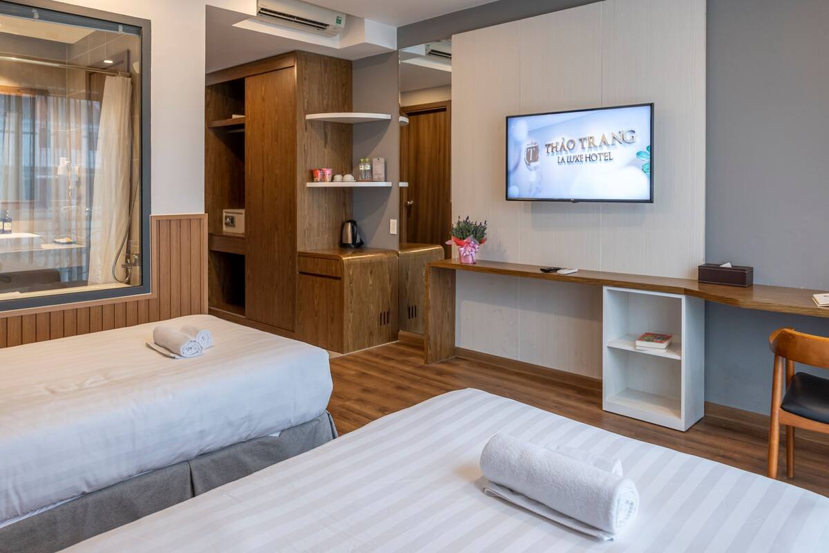 Habitación de hotel con dos camas, televisión, armario de madera y escritorio con silla.