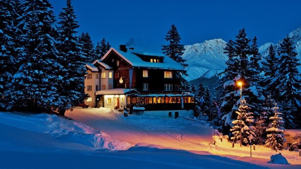 A large, multi-story lodge with a prominent entrance and a snow-covered landscape. - Hotel Arlenwald (Arosa)