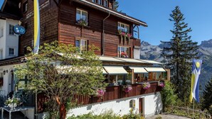 A wooden chalet with balconies, a restaurant area, and a mountain backdrop. - Hotel Arlenwald (Arosa)