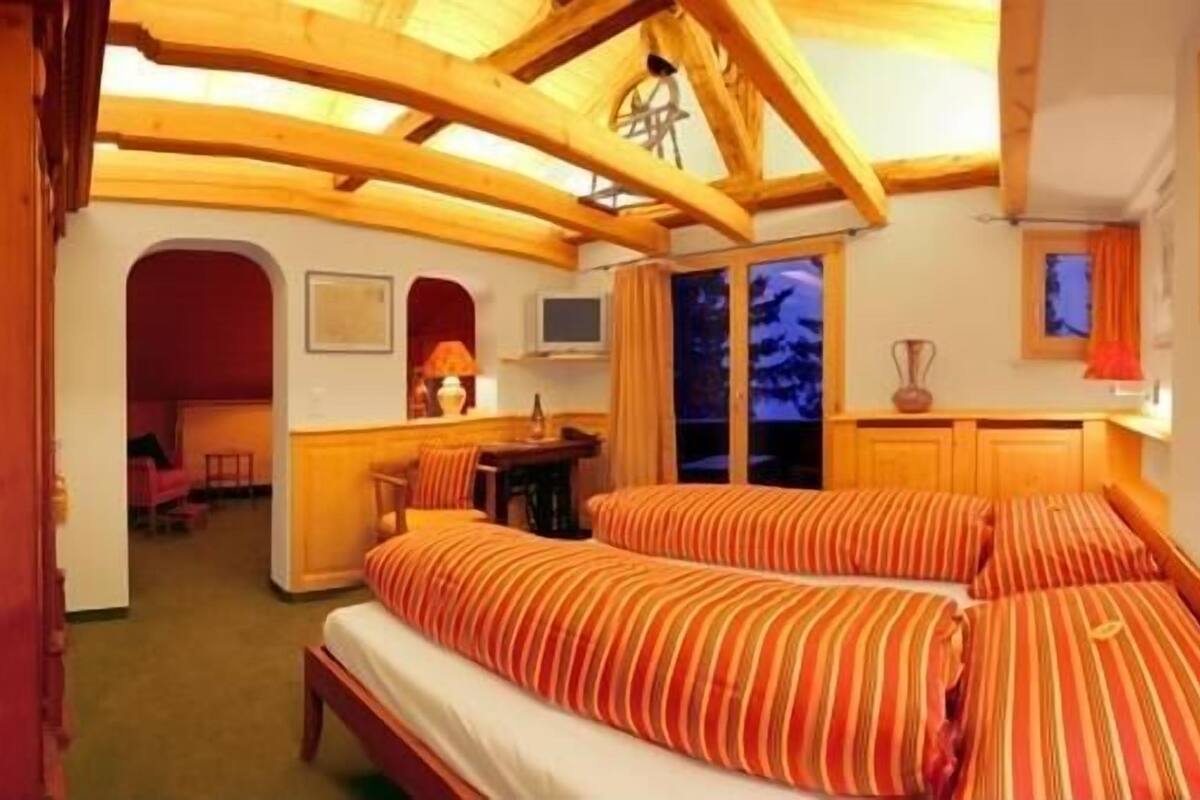 A cozy room with wooden beams, a bed with striped bedding, a desk with a lamp, and a TV.