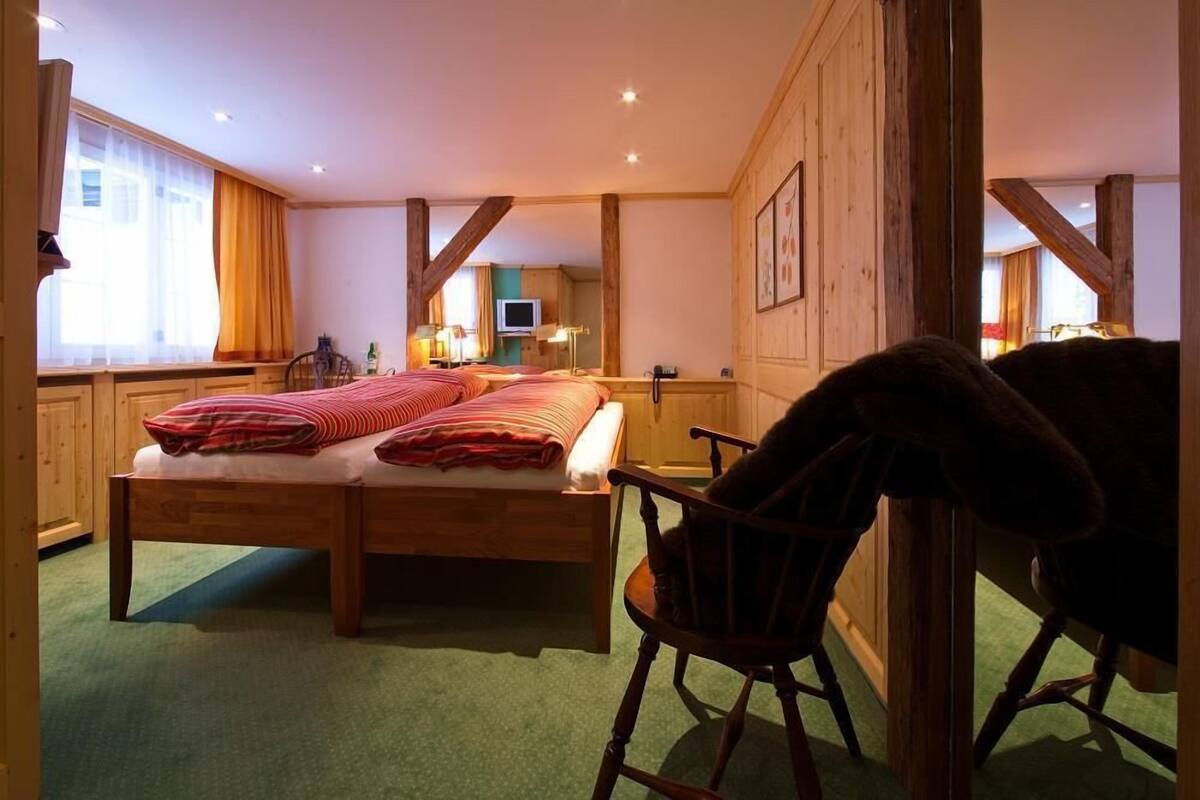 A cozy bedroom with a wooden bed, a rocking chair, and a large window with curtains.