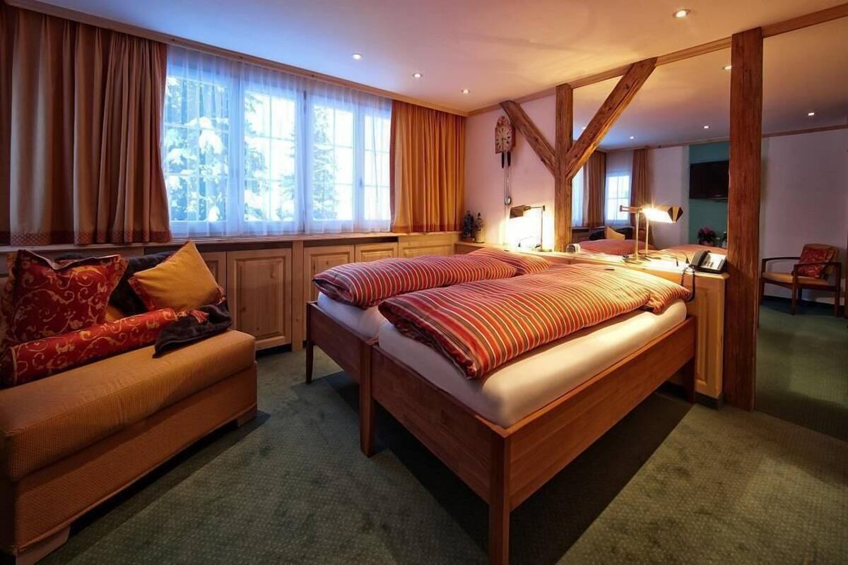 A bedroom with a large bed, a sofa, a desk, and a window with curtains.