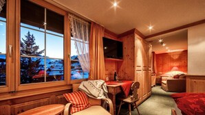 A cozy room with a wooden interior, a dining area, and a bed. - Hotel Arlenwald (Arosa)