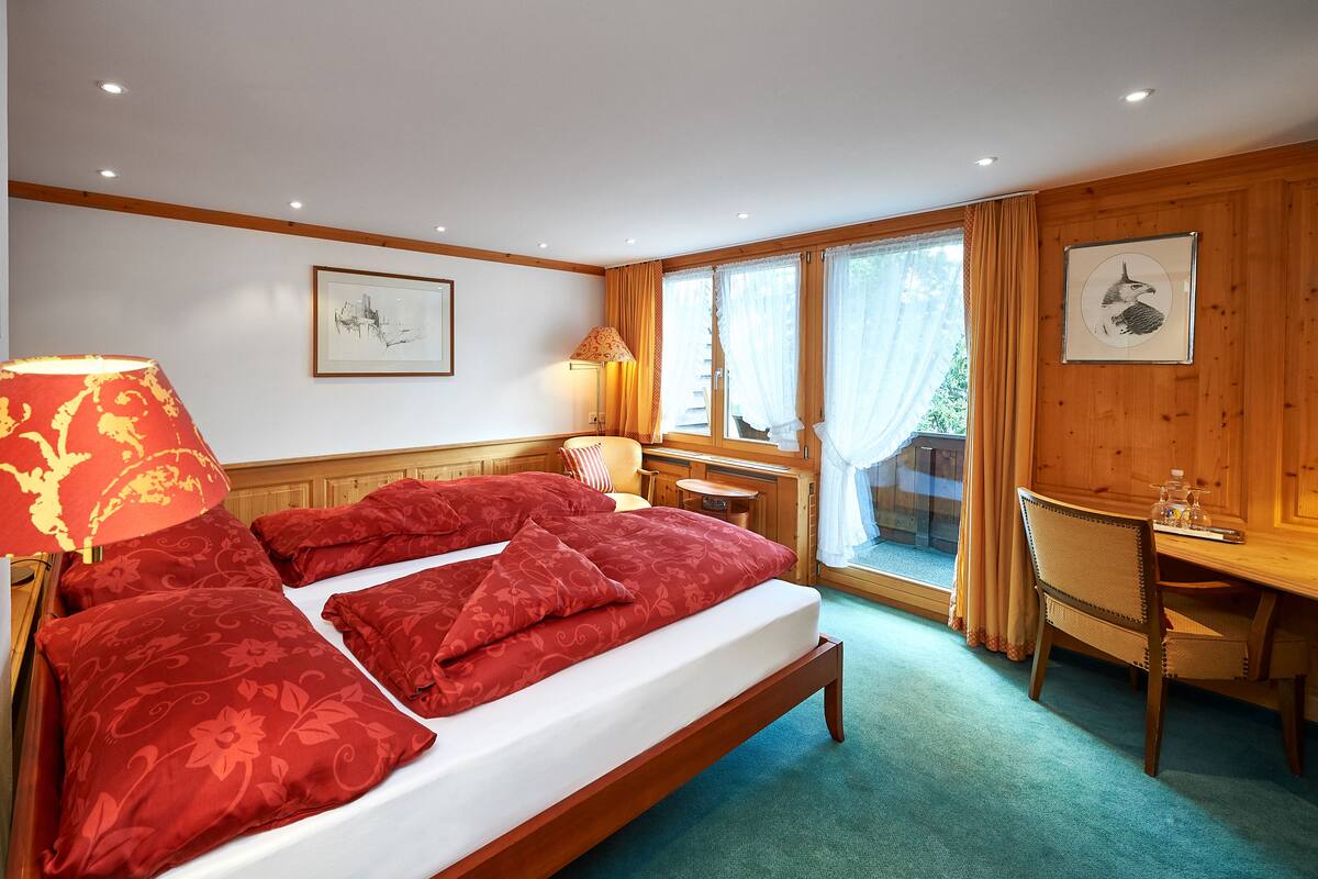 A hotel room with a wooden bed, a desk, a chair, and a window with curtains.