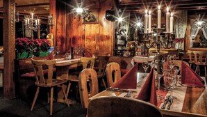 A cozy restaurant with wooden decor, candle-lit tables, and vintage teddy bears. - Hotel Arlenwald (Arosa)