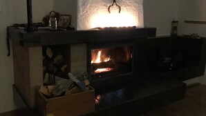 A fireplace with a lit fire, a mantel with various items, and a box of firewood on the floor. - Bed & Breakfast Obermumpf (Obermumpf)