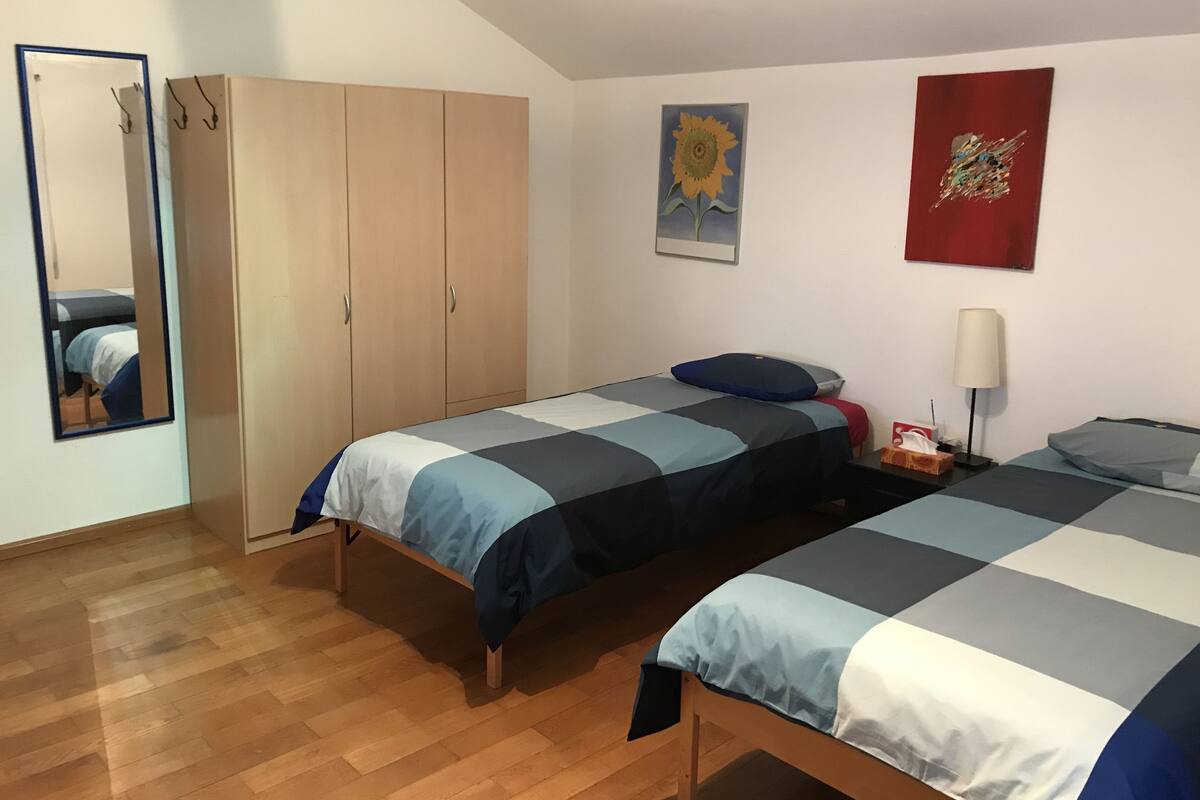 Un dormitorio con dos camas, armario de madera, espejo, obra de arte y una lámpara.