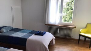 A bedroom with two beds, a window with curtains, a radiator, and a yellow chair. - Bed & Breakfast Obermumpf (Obermumpf)