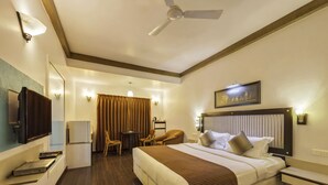 Una habitación de hotel con una cama grande, un escritorio, dos sillas, un televisor y un ventilador de techo.