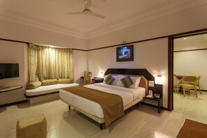 A hotel room with a large bed, bedside tables, a TV, a sofa, and a dining area. - Hotel Vrishali Executive Kolhapur (Kolhapur)