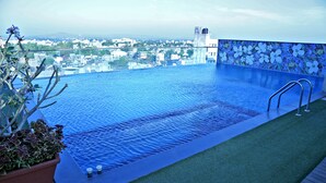 Una piscina infinita en la azotea con vistas despejadas del paisaje urbano, rodeada por un muro decorativo y plantas en macetas.