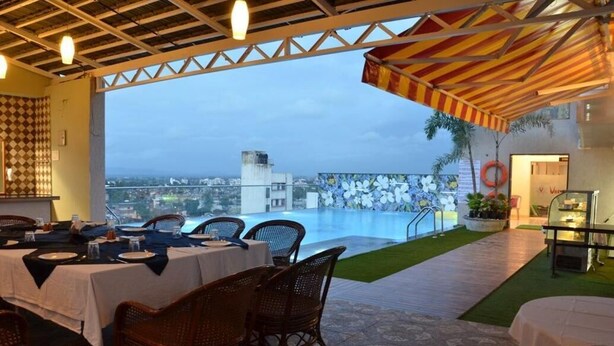 Un espacio para comer al aire libre con mesas y sillas, vistas a la ciudad y un ambiente junto a la piscina.
