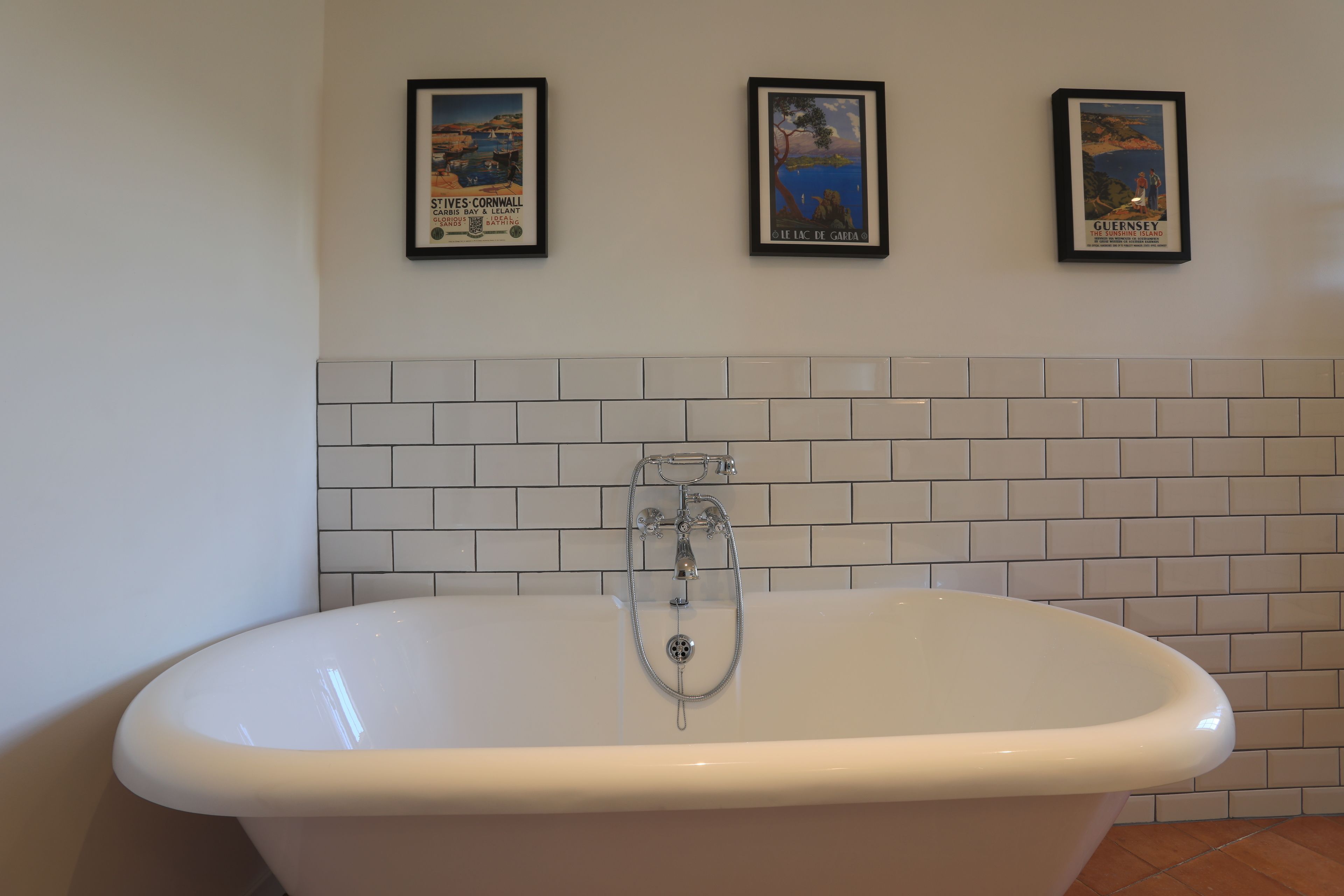 A bathroom with a freestanding bathtub, white tiled walls, and three framed posters on the wall.