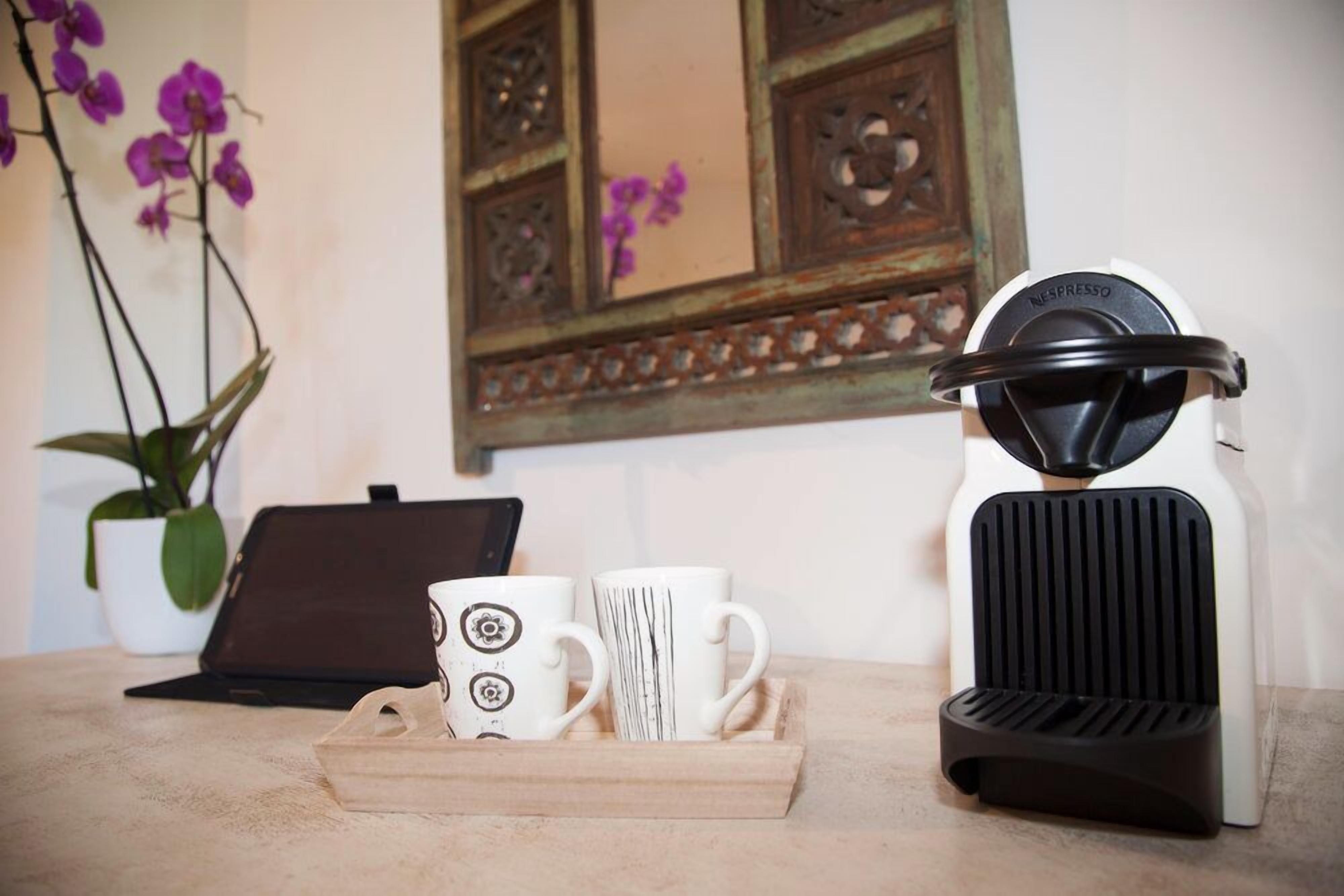 A coffee maker, two white mugs with black designs, and a laptop on a table with a wooden tray.