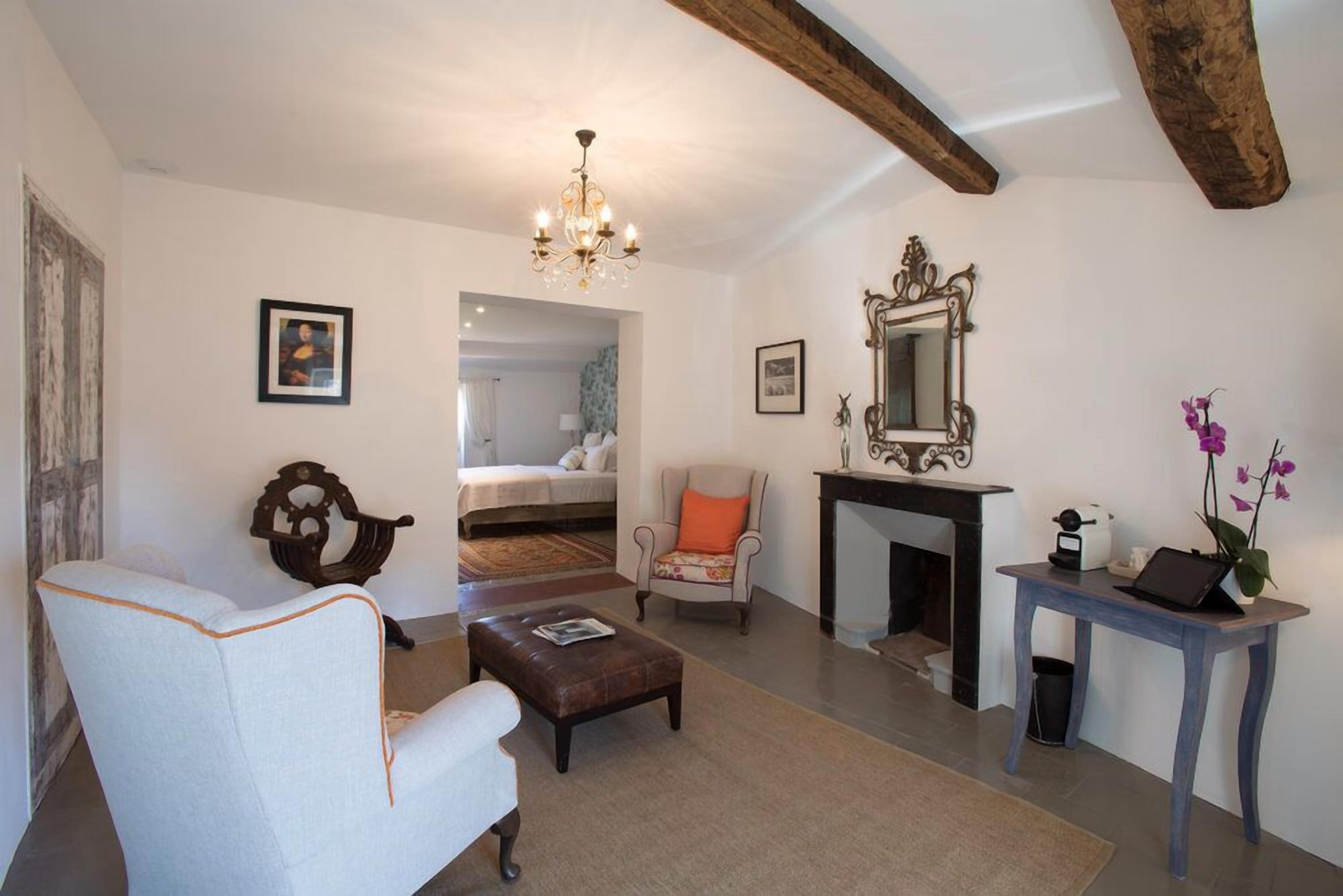 Een gezellige woonkamer met een witte fauteuil, een houten bankje, een open haard en een kleine tafel met een laptop.