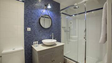 Un baño con inodoro blanco, lavabo con espejo redondo y ducha con cerramiento de vidrio.
