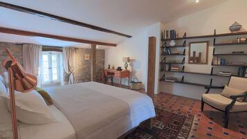 A bedroom with a large bed, a desk, a chair, a bookshelf, and a patterned rug.
