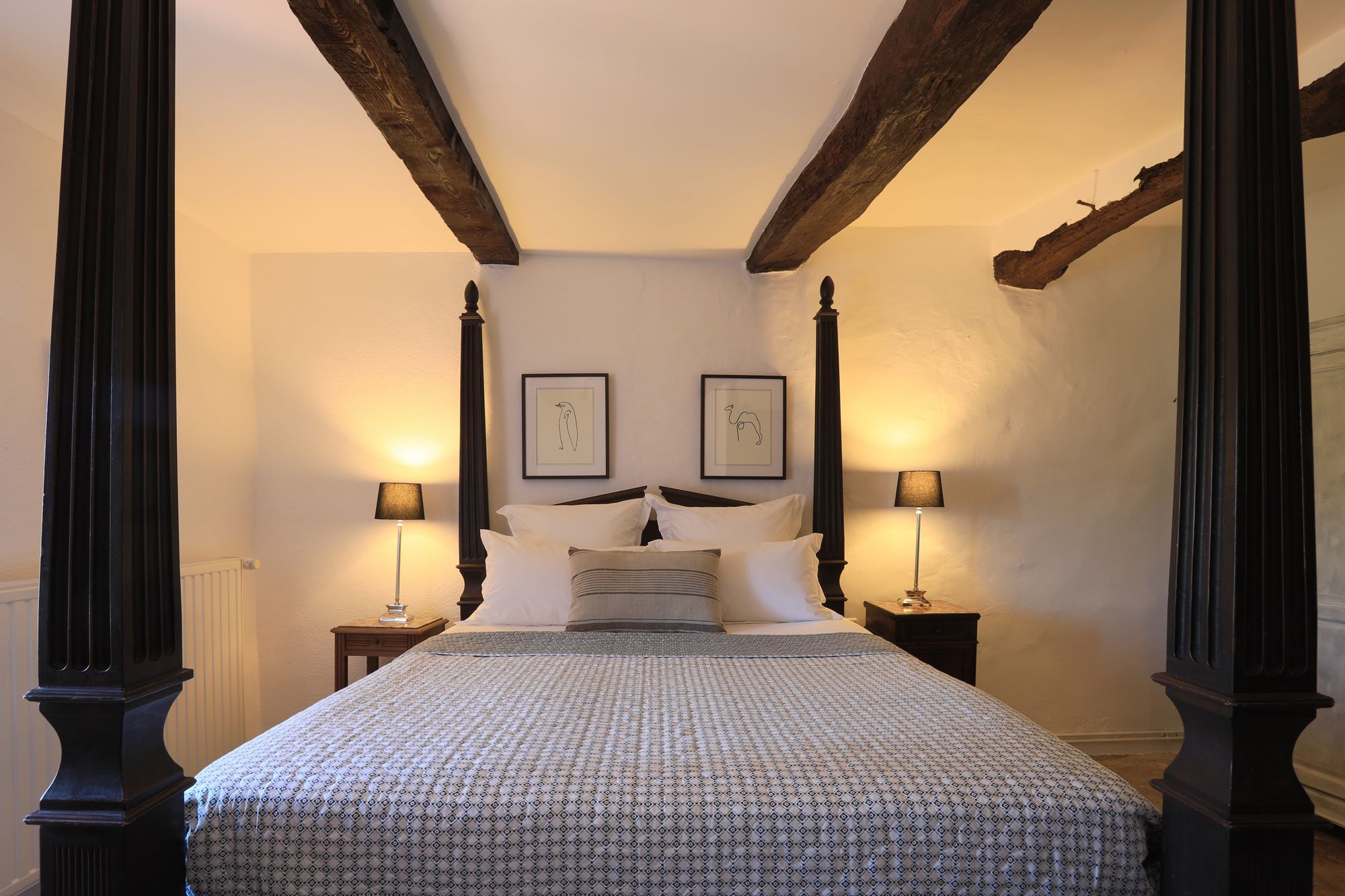 A bedroom with a four-poster bed, two bedside tables, and two wall-mounted lamps.