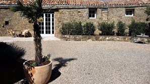 A stone building with a tiled roof, a gravel courtyard, and a potted palm tree. - Chateau d'Olmet Guesthouse (Olmet-et-Villecun)