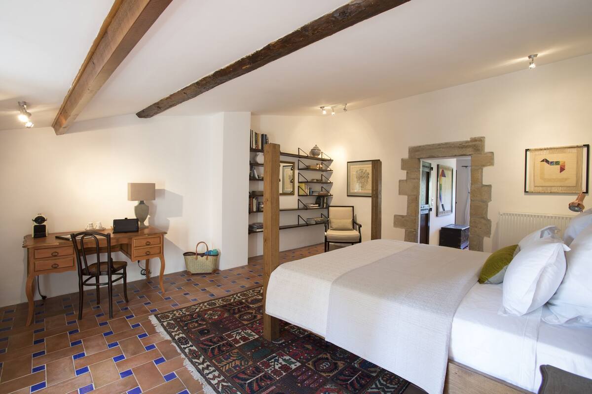 A bedroom with a bed, a desk, a chair, a bookshelf, and a patterned rug.