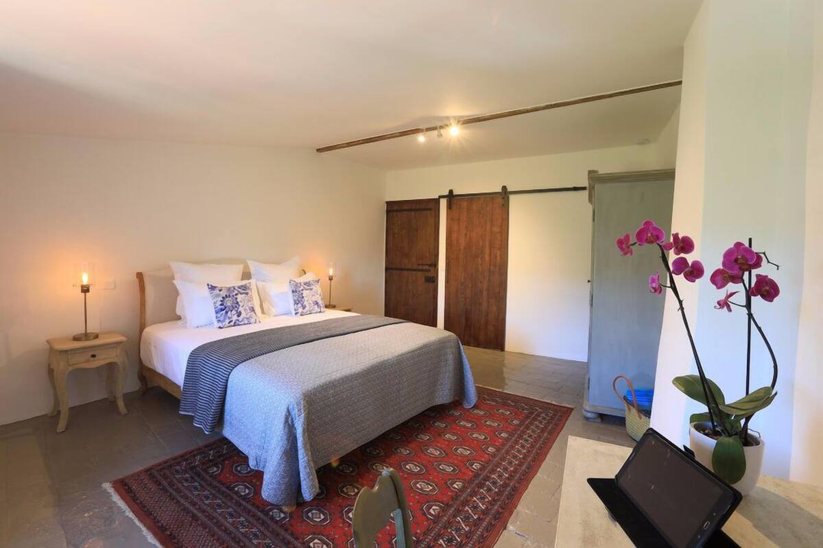 A bedroom with a bed, bedside table, lamp, and a potted orchid.
