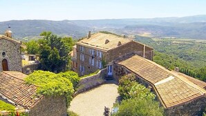 A stone building with a tiled roof, surrounded by greenery and hills in the background. - Chateau d'Olmet Guesthouse (Olmet-et-Villecun)