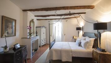 A bedroom with a bed, bedside table, lamp, dresser, mirror, and a potted plant.