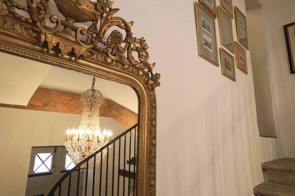 Una gran escalera con un espejo de marco ornamentado, un candelabro y cuadros en la pared.
