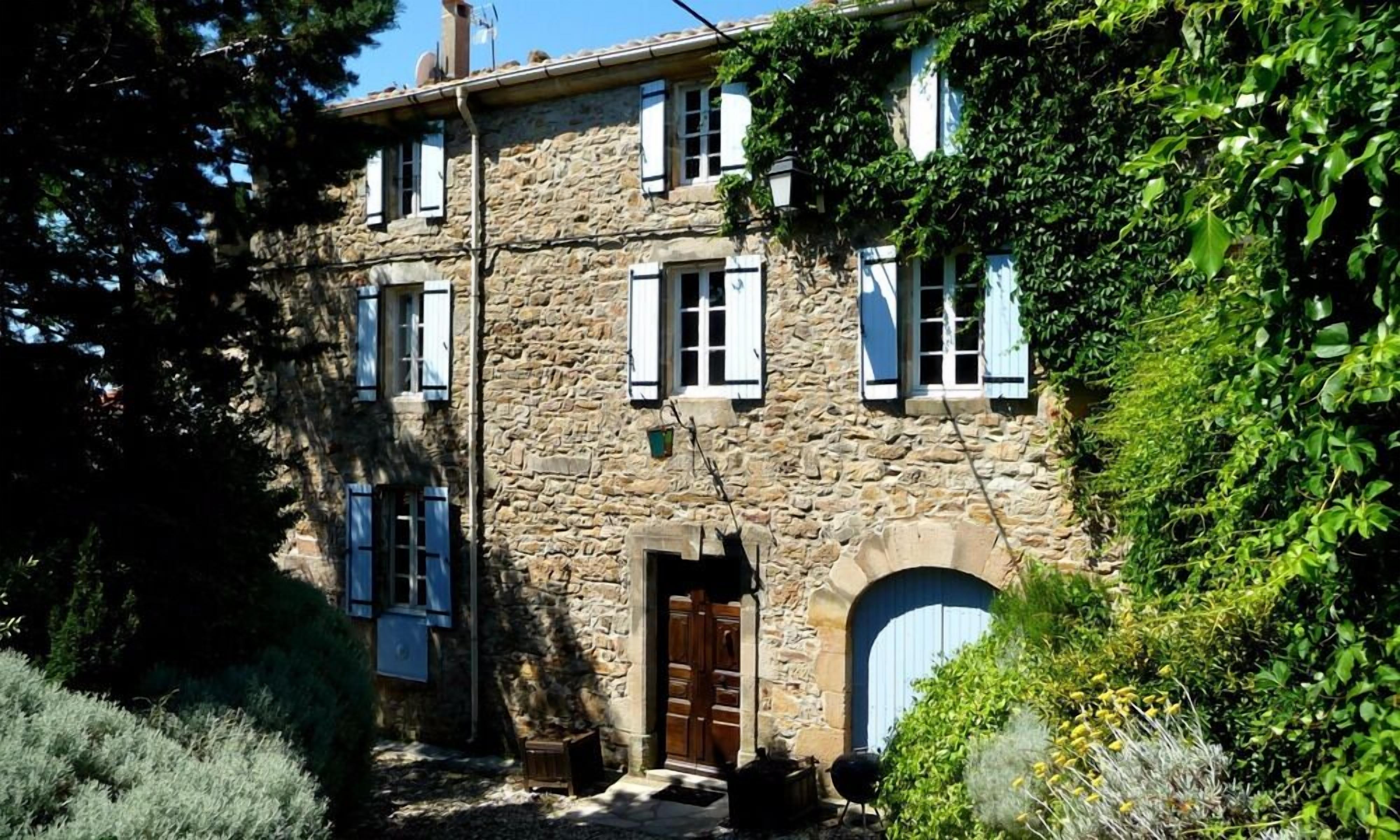 A stone building with a central entrance, multiple windows with shutters, and a door.