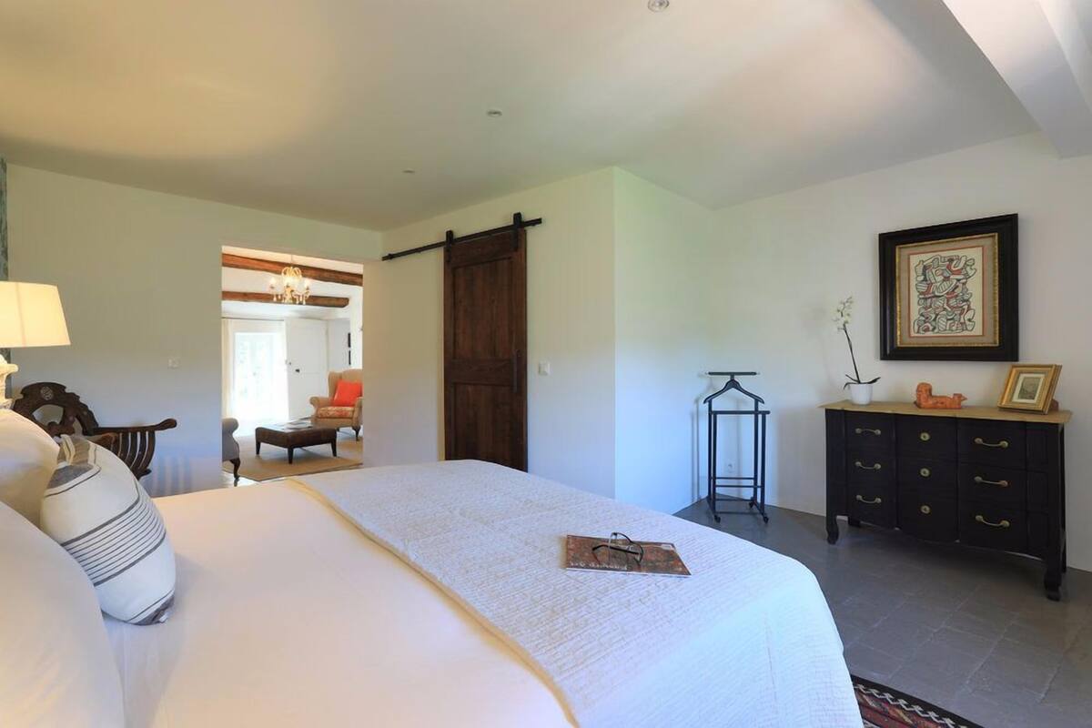 A bedroom with a large bed, a dresser, a chair, a desk, and a door.