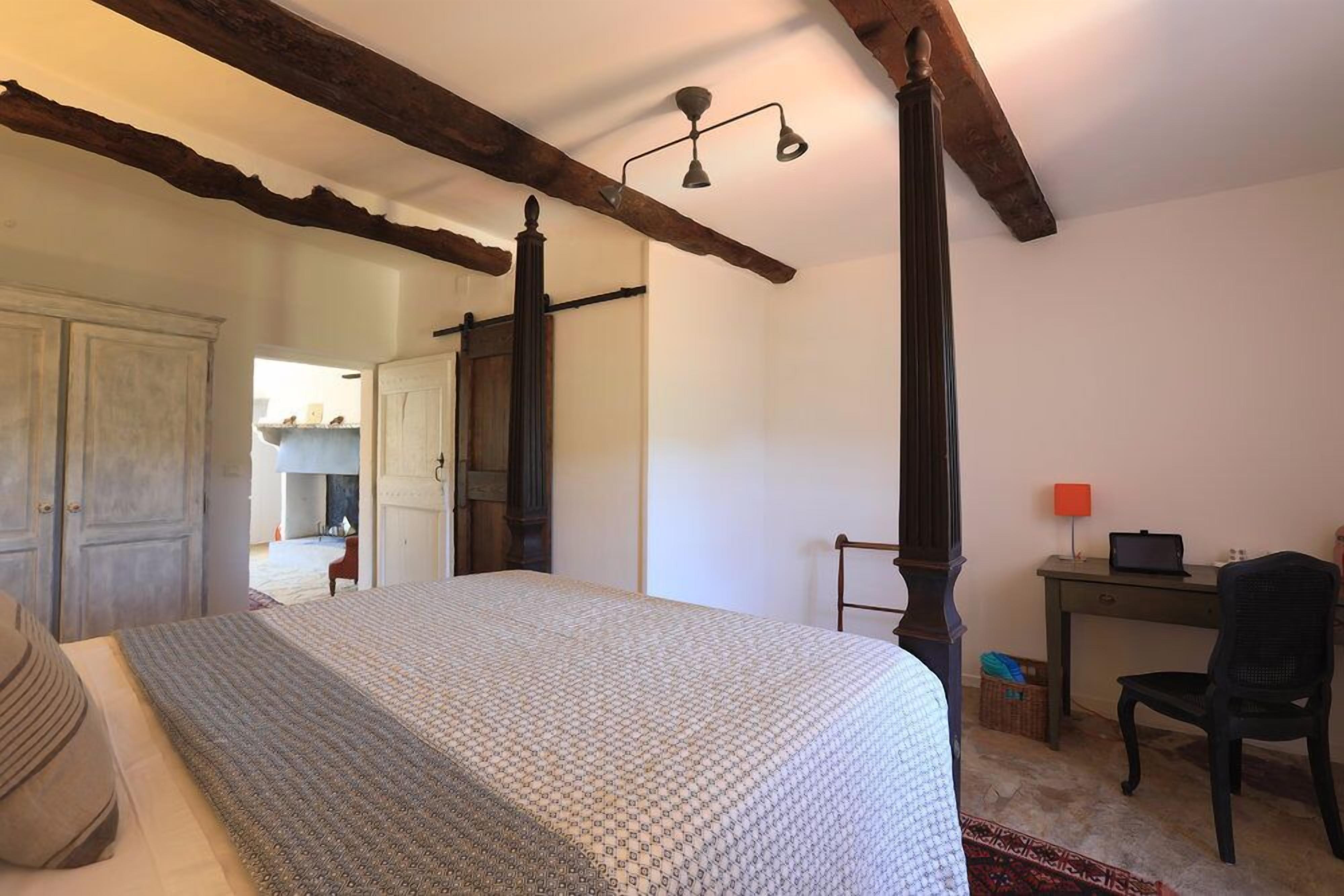 A bedroom with a four-poster bed, a desk with a laptop, and a chair.